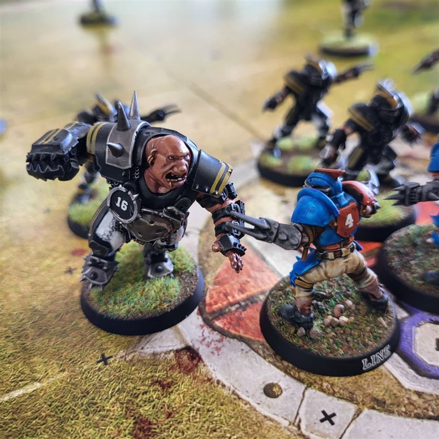 Painted Blood Bowl players, including an armoured ogre, lining up on the pitch